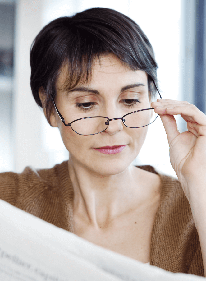 mature woman lowering glasses to read newspaper