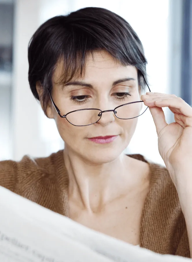 mature woman lowering glasses to read newspaper